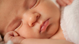 A close-up photograph of a sleeping newborn baby's face. It's a selective focus image, with the focus being on the infant's tiny lips.