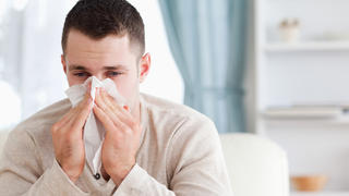 Man blowing his nose in his living room
