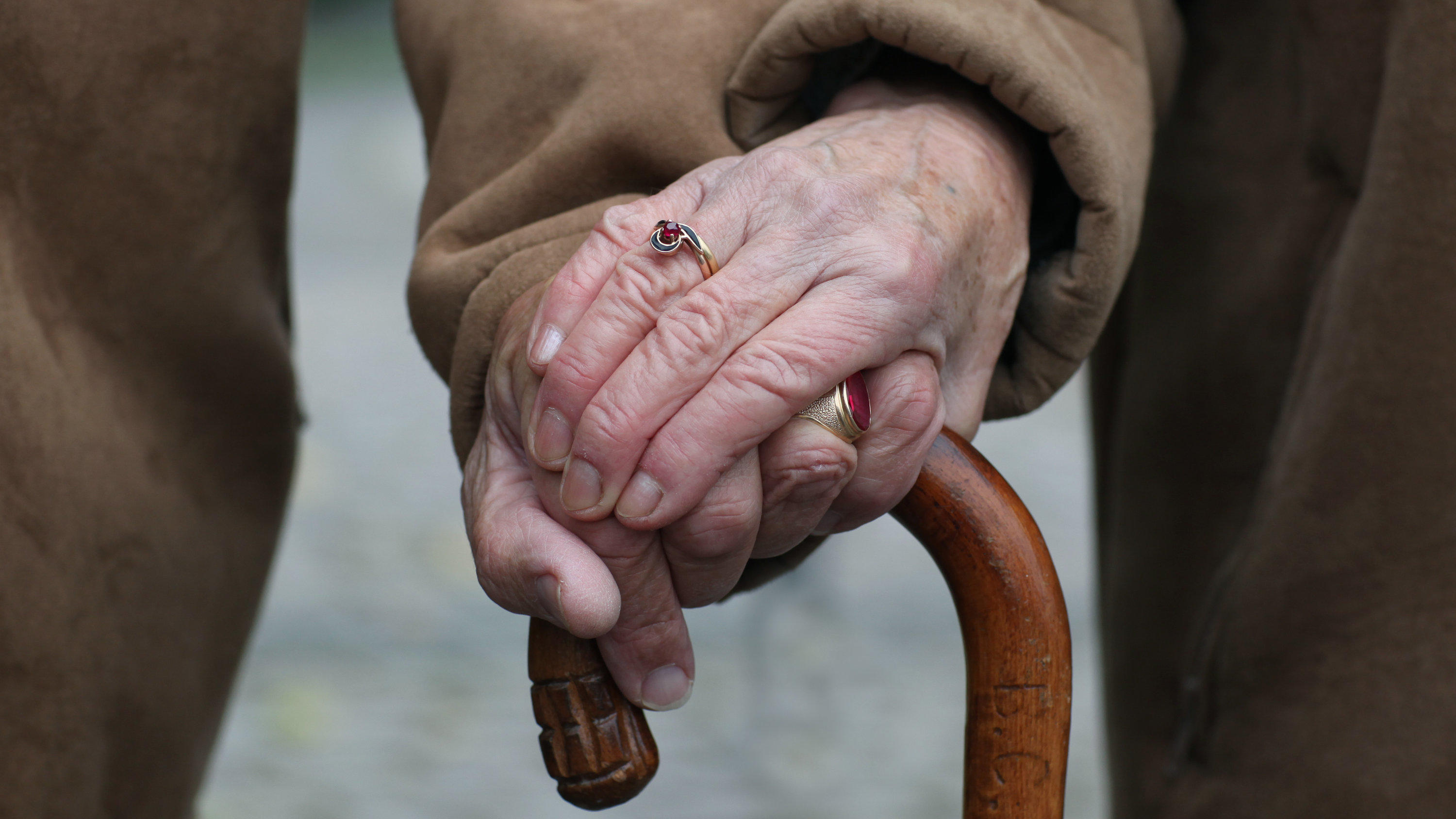Die Hände eines alten Ehepaares auf einen Stock gestützt.