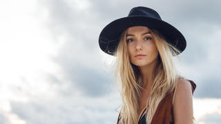 Close up of beautiful young blonde woman with black hat. Wearing brown vest. Her long messy hair looks amazing.
