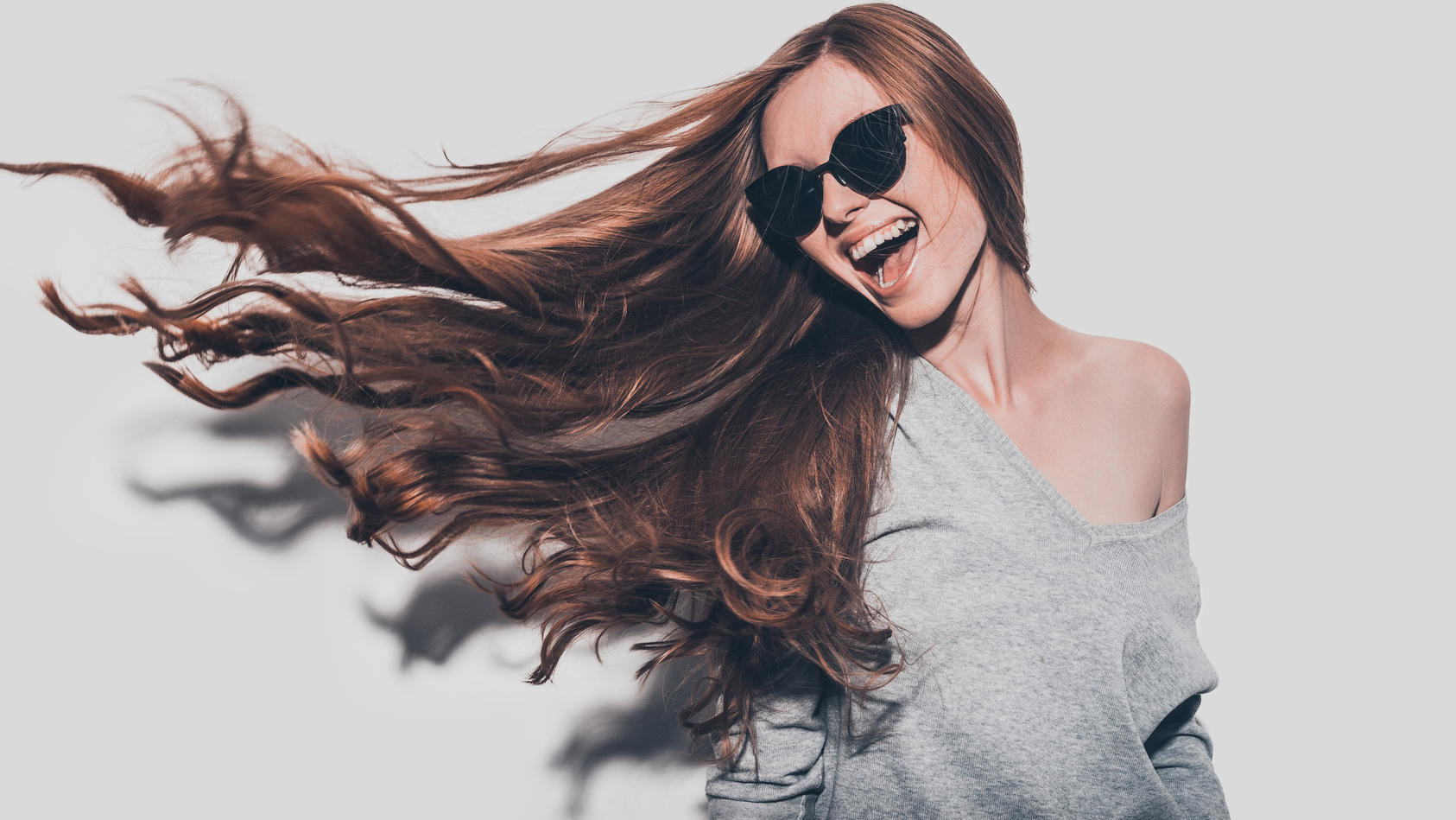 Junge Frau mit Sonnenbrille und langen Haaren lacht in die Kamera.