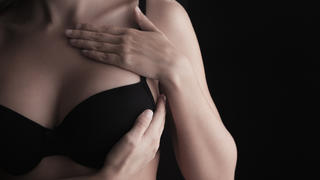 Breast examination - woman in black bra holding hands on breast. Copy space.