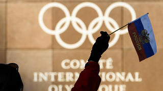 Eine Frau hält am 05.12.2017 eine russische Fahne vor den olympischen Ringen am Hauptquartierdes Internationalen Olympischen Komitees (IOC) in Lausanne (Schweiz). Das IOC wollte im Laufe des Tages über Strafen bis hin zu einem Ausschluss der Sport-Großmacht Russland von den Olympischen Winterspielen im Februar in Südkorea beraten. Möglich ist auch ein Verbot russischer Symbole wie der Fahne und der Hymne Foto: Jean-Christophe Bott/KEYSTONE/dpa +++(c) dpa - Bildfunk+++