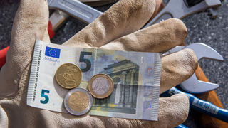 ARCHIV - ILLUSTRATION - Auf einer Hand mit einem Arbeitshandschuh sind am 26.02.2015 in Schwerin (Mecklenburg-Vorpommern) Euromünzen und einem Fünf-Euro-Geldschein mit einem Betrag von 8,50 Euro zu sehen (gestelltes Foto). Foto: Jens Büttner/dpa (zu dpa «IAB-Chef: Mindestlohn-Erhöhung kein Risiko für den Arbeitsmarkt» vom 23.06.2016) +++(c) dpa - Bildfunk+++