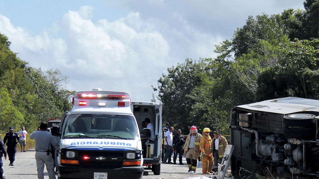 Polizisten, Sanitäter und Feuerwehrmänner stehen am 19.12.2017 in Mahahual (Mexiko) neben einem Opfer und dem umgestürzten Bus. Bei dem Unfall während eines Kreuzfahrt- Landausflugs in Mexiko sind zwölf Touristen ums Leben gekommen. Weitere 18 Mensch