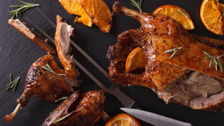 Cutting the roast duck and oranges closeup on a black slate board. horizontal view from above