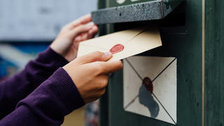 Eine Frauenhand holt einen Brief mit Siegel aus einem Postkasten.