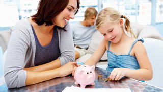 Pretty little girl putting money in piggy bank with her parents in the living room
