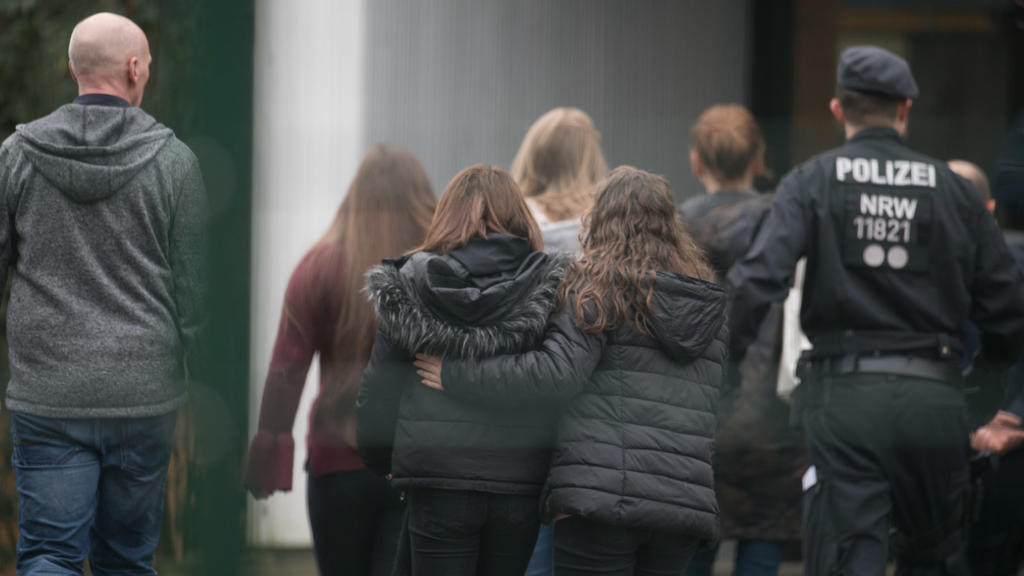 Polizisten begleiten am 23.01.2018 in Lünen (Nordrhein-Westfalen) Kinder über den Pausenhof der Käthe Kollwitz Gesamtschule. Ein Schüler soll von einem Mitschüler getötet worden sein. Ein minderjähriger Tatverdächtiger wurde im Rahmen einer Fahndung
