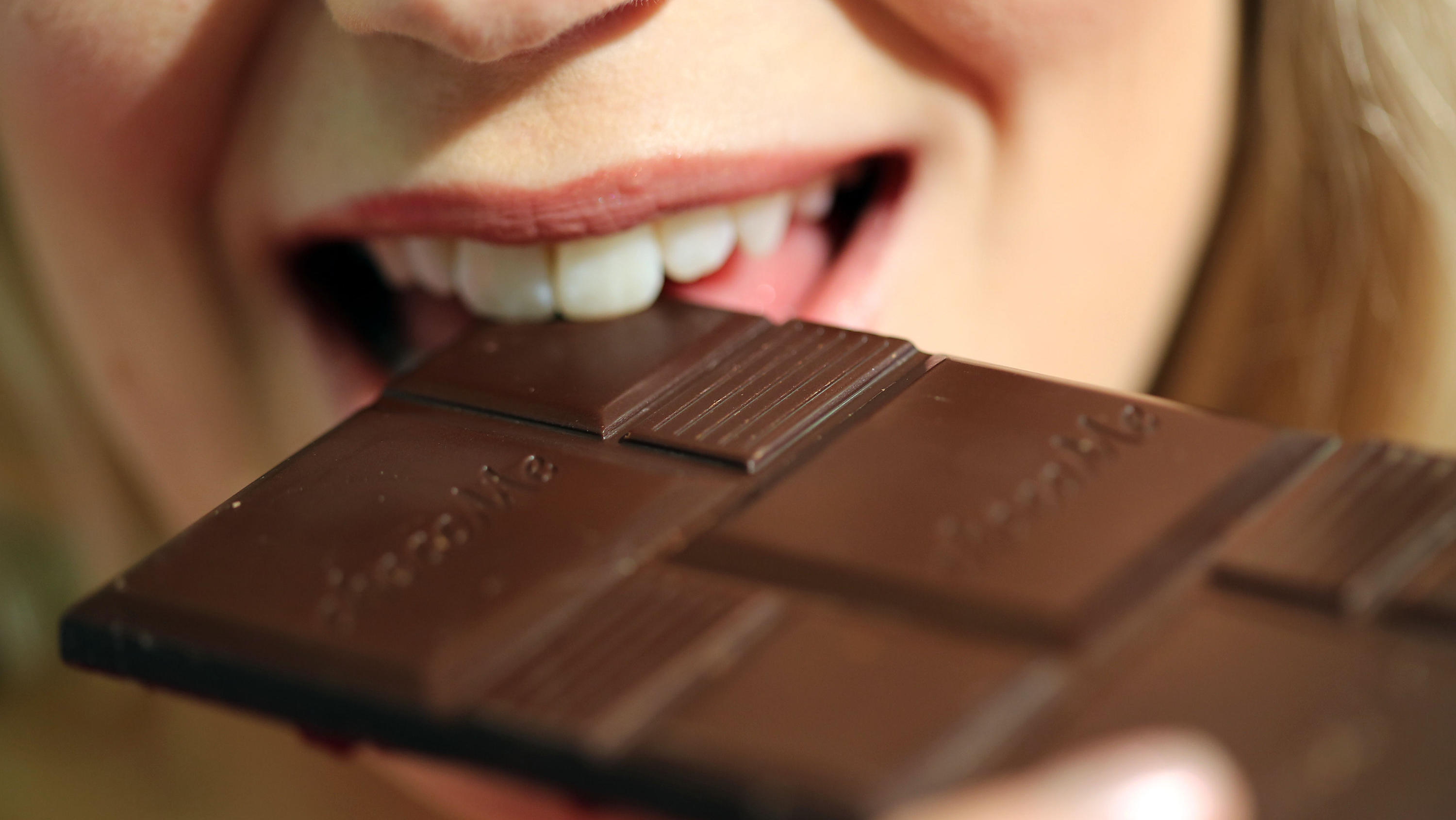 Ein weibliches Model beißt in eine große Tafel Schokolade.