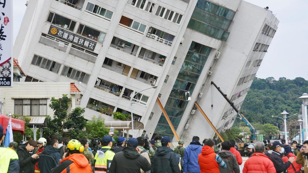 dpatopbilder - 07.02.2018, Taiwan, Hualien: Schaulustige versammeln sich vor dem nach einem Erdbeben eingestürzten und nun schief stehenden Yuntsui Building. Ein Erdbeben mit einer Stärke von 6,4 hat sich am 06.02.2018 (Ortszeit/16.50 Uhr MEZ) in Tai