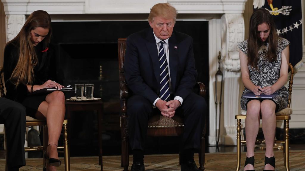 U.S. President Donald Trump bows his head during a prayer as he sits between Marjory Stoneman Douglas High School shooting survivors and students Julia Cordover (L) and Carson Abt (R) as the president hosts a listening session with high school studen