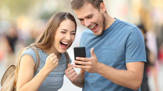 Excited couple receiving good news on line in a smart phone outside on the street