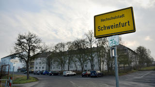 27.03.2018, Bayern, Schweinfurt: Blick auf das Ortsschild von Schweinfurt. Die Polizei hatte am Vortag Chemikalien in einer Sozialunterkunft entdeckt (mittleres Gebäude im Hintergrund), die für den Bau von Rohrbomben geeignet gewesen wären. Foto: Nicolas Armer/dpa +++ dpa-Bildfunk +++