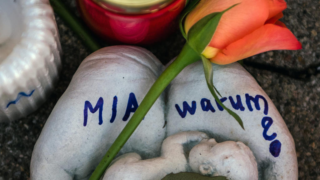 ARCHIV - 28.12.2017, Rheinland-Pfalz, Kandel: Eine Skulptur in Form zweier Handflächen mit der Aufschrift "Mia warum?" und eine Rose liegen vor dem Drogeriemarkt, in dem ein 15-jähriges Mädchen von ihrem Ex-Freund erstochen wurde. (zu dpa «Mordankla