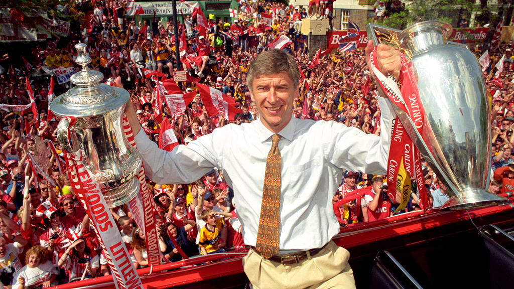 ARCHIV - 17.05.1998, Großbritannien, London: Arsène Wenger, Trainer des FC Arsenal, hält die Pokale vom FA Cup und vom League Cup, während im Hintergrund die Fans jubeln. Arsène Wenger hört nach fast 22 Jahren als Trainer des FC Arsenal am Ende diese