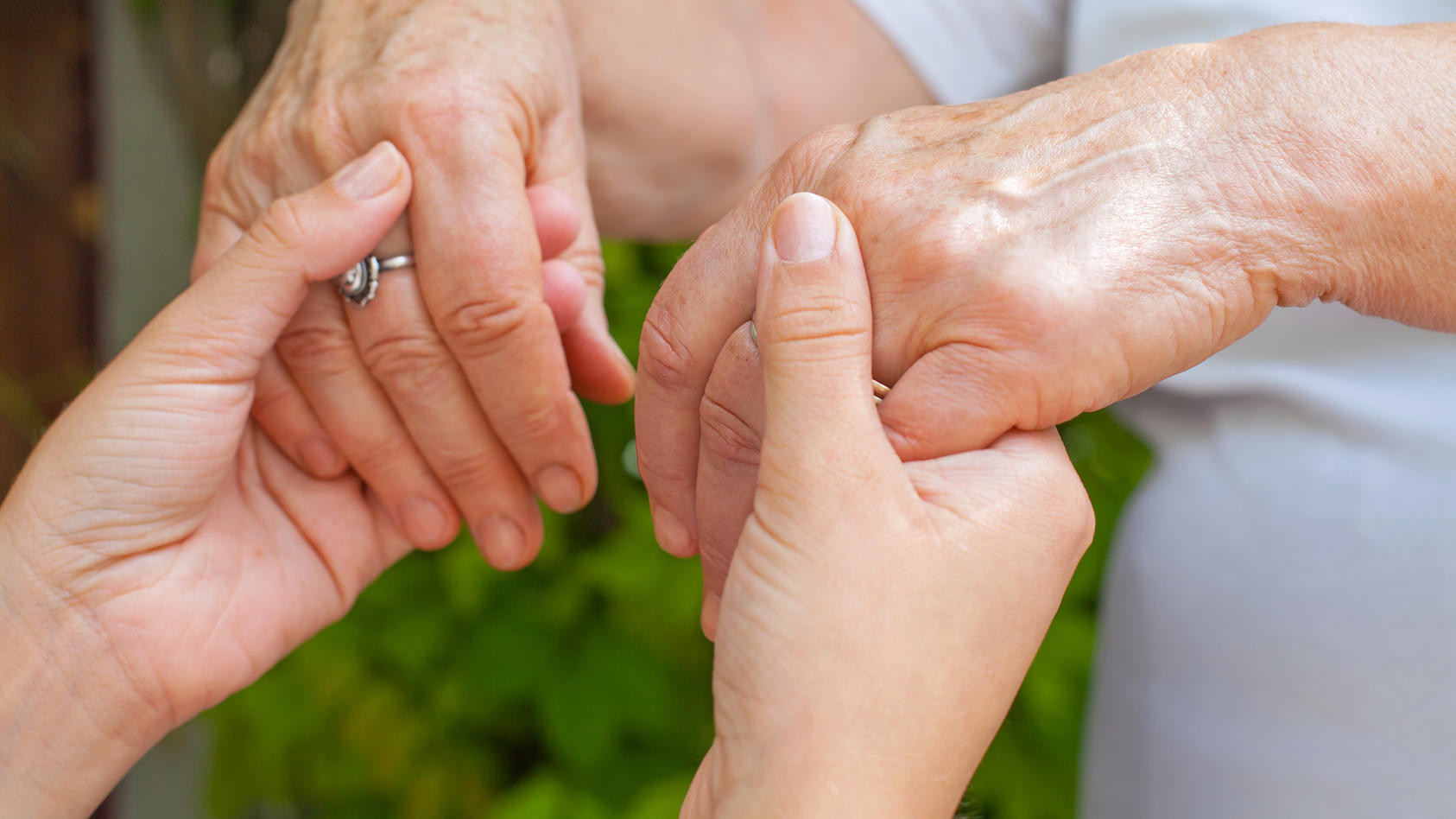 Close up young caregiver holding elderly female's trembling hands, Parkinson disease