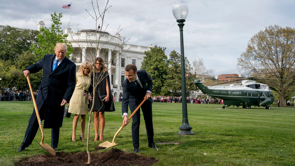 ARCHIV - 23.04.2018, USA, Washington: Donald Trump (l), Präsident der USA, und Emmanuel Macron, Präsident von Frankreich, pflanzen gemeinsam eine Eiche vor dem Weißen Haus. Brigitte Macron, Frau des Präsidenten von Frankreich, und die First Lady der