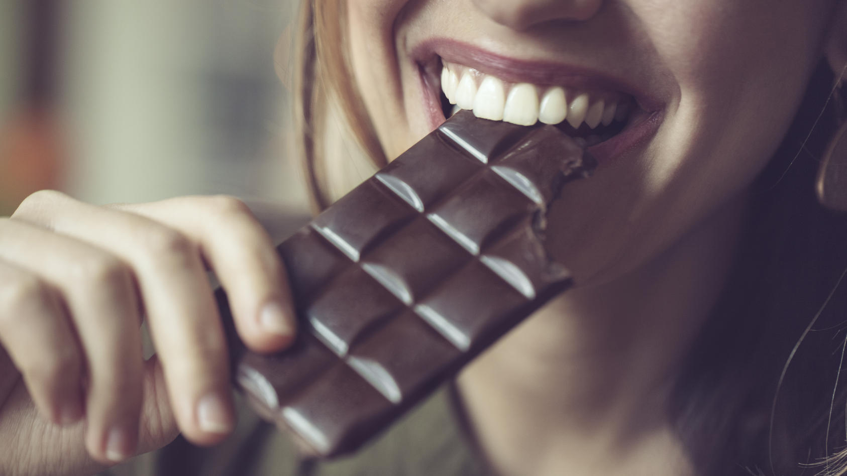 Junge Frau beißt lächelnd in eine Tafel Bitterschokolade.