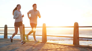 Junger Mann und junge Frau joggen gemeinsam vor Sonnenuntergang am Meer