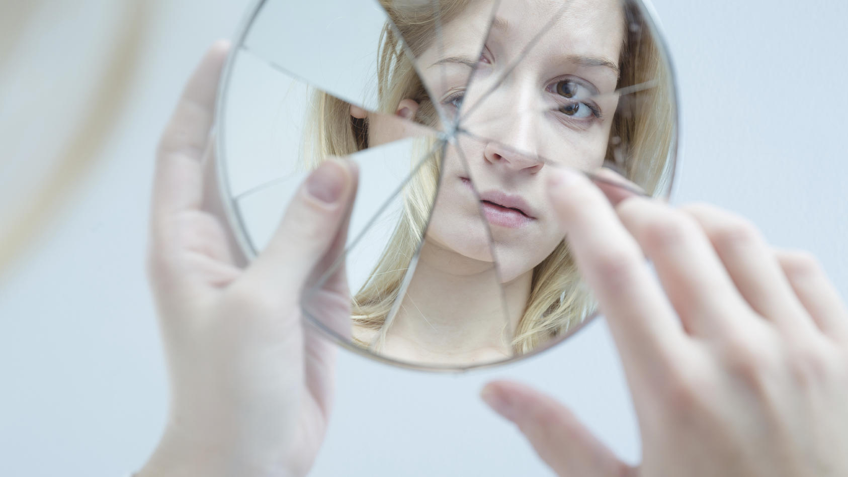 Junge Frau betrachtet sich in einem zerbrochenen Spiegel.